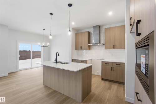 Kitchen featuring modern cabinets, hanging lights, an island with sink, light stone counters, and light wood-style floors - 19348 29 Avenue, Edmonton, AB - Indoor Photo Showing Kitchen With Double Sink With Upgraded Kitchen