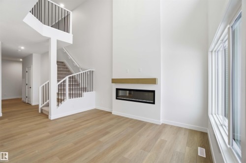 Unfurnished living room with a glass covered fireplace, light wood-style flooring, a high ceiling, and recessed lighting - 19348 29 Avenue, Edmonton, AB - Indoor With Fireplace