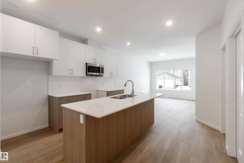 Kitchen with a center island with sink, two tone cabinets, light wood-style floors, recessed lighting, and stainless steel microwave - 18912 28 Avenue, Edmonton, AB - Indoor Photo Showing Kitchen With Double Sink