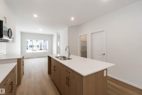Kitchen featuring light wood-type flooring, stainless steel microwave, a center island with sink, modern cabinets, and recessed lighting - 18912 28 Avenue, Edmonton, AB - Indoor Photo Showing Kitchen With Double Sink