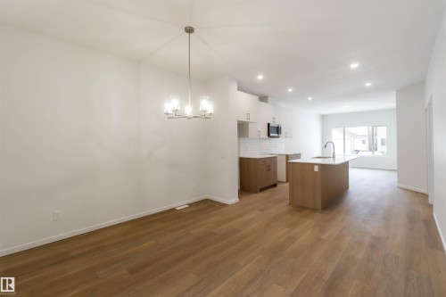 Dual tone kitchen with a kitchen island with sink, dark wood-style flooring, backsplash, a chandelier, and stainless steel microwave - 18912 28 Avenue, Edmonton, AB - Indoor Photo Showing Kitchen