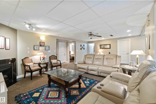 Carpeted living area with a paneled ceiling, ceiling fan, and a fireplace - 6116 53 Avenue, Beaumont, AB - Indoor Photo Showing Living Room With Fireplace
