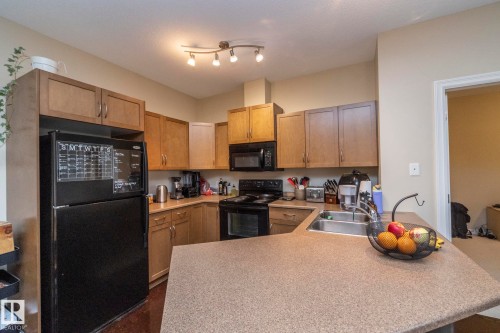 Kitchen with black appliances, light countertops, brown cabinetry, and a peninsula - 416 263 Macewan Road, Edmonton, AB - Indoor Photo Showing Kitchen With Double Sink