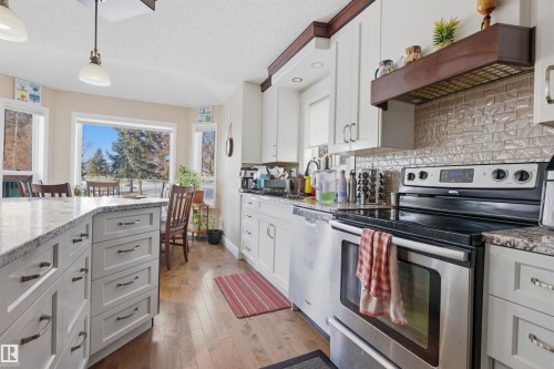 Kitchen featuring stainless steel appliances, white cabinets, light wood-type flooring, light stone countertops, and tasteful backsplash - 444 Breckenridge Lane Nw, Edmonton, AB - Indoor Photo Showing Kitchen With Upgraded Kitchen