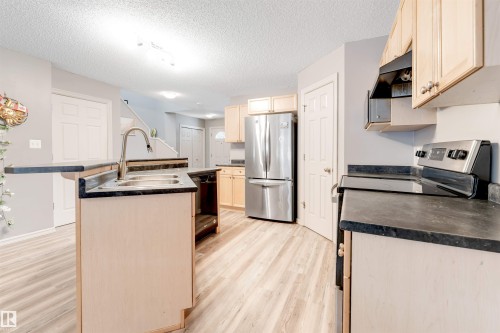 Kitchen featuring stainless steel appliances, an island with sink, dark countertops, light wood finished floors, and a textured ceiling - 1157 37 Avenue, Edmonton, AB - Indoor Photo Showing Kitchen