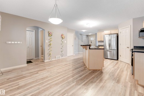 Kitchen with arched walkways, freestanding refrigerator, a center island with sink, dark countertops, and light wood finish cabinets - 1157 37 Avenue, Edmonton, AB - Indoor Photo Showing Kitchen