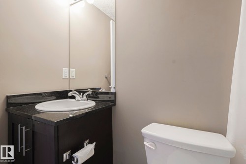 Bathroom featuring a dark vanity with a white basin and granite countertop, a wall-mounted mirror, and a toilet - 313 1510 Watt Drive, Edmonton, AB - Indoor Photo Showing Bathroom