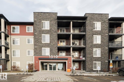 The property features a multi-story exterior with a combination of stone veneer and siding, private balconies with dark railings, and a prominent main entrance with large glass doors - 313 1510 Watt Drive, Edmonton, AB - Outdoor With Balcony With Facade