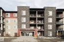 The property features a multi-story exterior with a combination of stone veneer and siding, private balconies with dark railings, and a prominent main entrance with large glass doors - 313 1510 Watt Drive, Edmonton, AB  - Outdoor With Balcony With Facade 