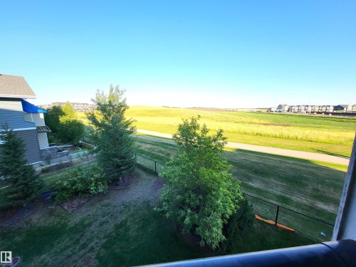 The property features a spacious yard with mature trees and a black fence, bordering an expansive open field with a paved pathway - 313 1510 Watt Drive, Edmonton, AB - Outdoor With View