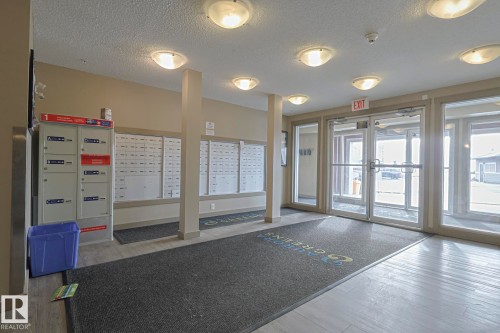 The property features a well-lit entrance with overhead lighting, a mail area, and glass doors providing natural light - 313 1510 Watt Drive, Edmonton, AB - Indoor Photo Showing Other Room