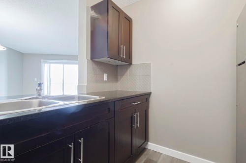 Kitchen with dark wood cabinetry, a double basin sink, and granite countertops - 313 1510 Watt Drive, Edmonton, AB - Indoor Photo Showing Kitchen With Double Sink