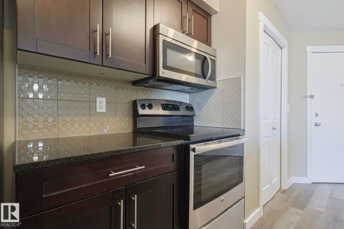The kitchen features dark wood cabinetry, a stainless steel microwave and oven, and a patterned backsplash - 313 1510 Watt Drive, Edmonton, AB - Indoor Photo Showing Kitchen