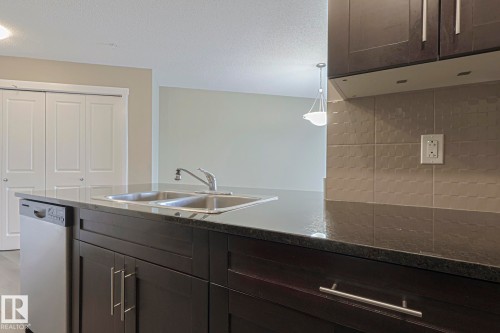 Kitchen featuring dark cabinetry, stainless steel dishwasher, double basin sink, and a tiled backsplash - 313 1510 Watt Drive, Edmonton, AB - Indoor Photo Showing Kitchen With Double Sink