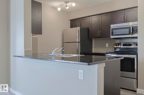 Kitchen featuring dark wood cabinetry, a stainless steel refrigerator, and a stainless steel oven and microwave - 313 1510 Watt Drive, Edmonton, AB - Indoor Photo Showing Kitchen With Stainless Steel Kitchen With Double Sink