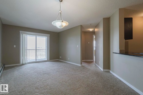 The living area features neutral-toned carpet flooring, light-colored walls, and a glass sliding door leading to an exterior balcony with a metal railing - 313 1510 Watt Drive, Edmonton, AB - Indoor Photo Showing Other Room