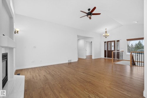 Unfurnished living room featuring a ceiling fan, a chandelier, dark wood-style floors, lofted ceiling, and a tiled fireplace - 19 Country Lane, Stony Plain, AB - Indoor With Fireplace