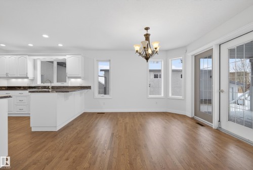 Kitchen featuring white cabinetry, light wood-style flooring, a peninsula, dark stone counters, and suspended lighting - 19 Country Lane, Stony Plain, AB - Indoor Photo Showing Kitchen With Upgraded Kitchen