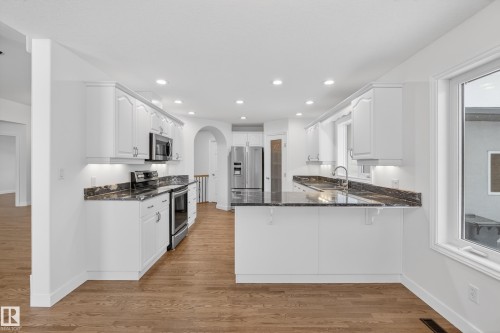 Kitchen with dark stone countertops, white cabinetry, stainless steel appliances, a peninsula, and arched walkways - 19 Country Lane, Stony Plain, AB - Indoor Photo Showing Kitchen With Upgraded Kitchen