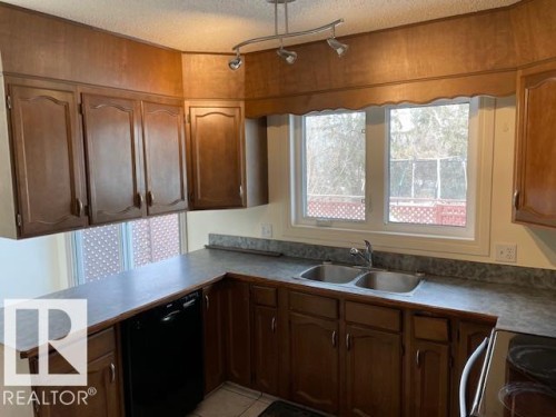Kitchen featuring black appliances, a textured ceiling, a peninsula, light tile patterned floors, and wood finish cabinets - 11 Campbell, Stony Plain, AB - Indoor Photo Showing Kitchen With Double Sink