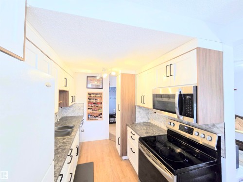 Kitchen with stainless steel appliances, a textured ceiling, light wood-style floors, white cabinetry, and decorative backsplash - 80 Amberly Crest, Edmonton, AB - Indoor Photo Showing Kitchen