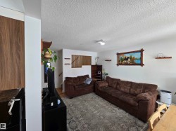Spacious living area featuring white walls, a textured ceiling, and wood accents - 