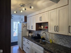 The kitchen features white cabinetry with black hardware, a dual basin stainless steel sink, a tiled backsplash, and track lighting - 