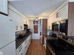 The kitchen features white cabinetry with black hardware, a stainless steel microwave and stove, and light wood flooring - 