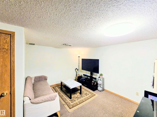 Carpeted living area featuring a textured ceiling and baseboards - 2 4403 Riverbend Road, Edmonton, AB - Indoor