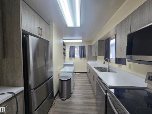 Galley kitchen featuring wood-grain cabinetry, stainless steel appliances, and wood-finish flooring - 2 4403 Riverbend Road, Edmonton, AB 