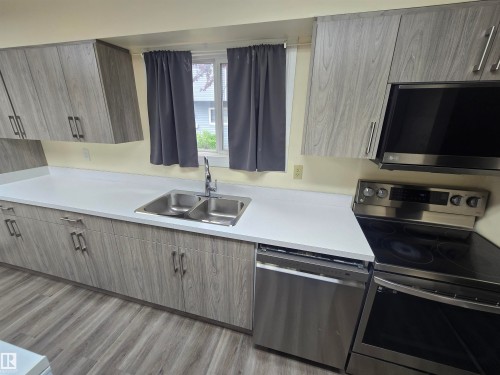 Kitchen featuring wood-finish cabinetry with modern hardware, light-toned countertops, a stainless steel double basin sink, and wood-finish flooring - 2 4403 Riverbend Road, Edmonton, AB 