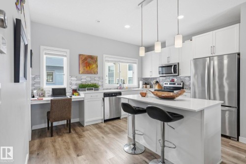 Kitchen with white cabinets, stainless steel appliances, a kitchen island, a breakfast bar area, and tasteful backsplash - 90 1010 Rabbit Hill Road, Edmonton, AB - Indoor Photo Showing Kitchen With Stainless Steel Kitchen With Upgraded Kitchen