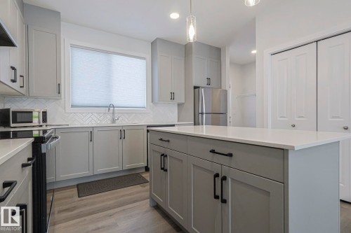 Kitchen with gray cabinets, stainless steel appliances, light wood-style floors, hanging light fixtures, and backsplash - 3520 Kulay Link Link, Edmonton, AB - Indoor Photo Showing Kitchen With Upgraded Kitchen