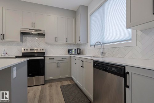 Kitchen featuring stainless steel appliances, light wood-type flooring, light stone counters, gray cabinetry, and tasteful backsplash - 3520 Kulay Link Link, Edmonton, AB - Indoor Photo Showing Kitchen With Upgraded Kitchen