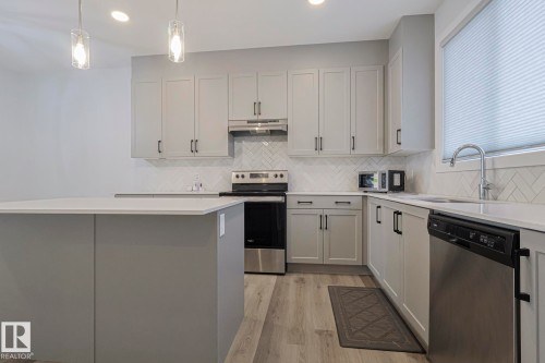 Kitchen featuring stainless steel appliances, light wood-type flooring, hanging light fixtures, a center island, and light stone countertops - 3520 Kulay Link Link, Edmonton, AB - Indoor Photo Showing Kitchen With Upgraded Kitchen