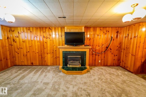 Unfurnished living room with carpet flooring, a tiled fireplace, and wooden walls - 4812 51 Avenue, Vilna, AB - Indoor Photo Showing Other Room With Fireplace