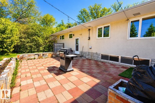 Expansive paver patio with a two-tone brick pattern, bordered by a stone retaining wall and lush green foliage - 4812 51 Avenue, Vilna, AB - Outdoor