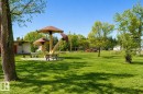 Expansive lawn with mature trees, featuring a distinct mushroom-themed play structure and multiple park benches - 4812 51 Avenue, Vilna, AB  - Outdoor 