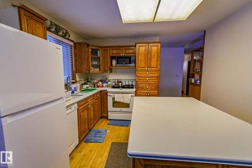 Kitchen with white appliances, wood finish cabinetry, light wood-style floors, and light countertops - 4812 51 Avenue, Vilna, AB - Indoor Photo Showing Kitchen