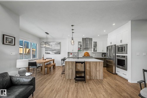 Kitchen with dual tone cabinets, stainless steel appliances, glass fronted cabinets, a kitchen island with sink, and light wood-style floors - 34 Riverhill Crescent, St. Albert, AB - Indoor Photo Showing Other Room