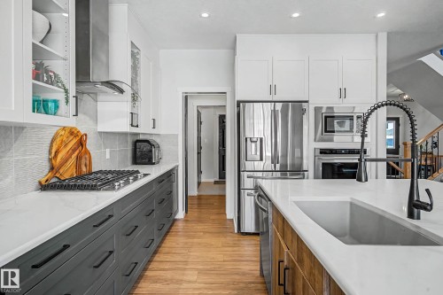 Two tone kitchen with two tone color scheme, light wood-style flooring, stainless steel appliances, light stone countertops, and backsplash - 34 Riverhill Crescent, St. Albert, AB - Indoor Photo Showing Kitchen With Upgraded Kitchen