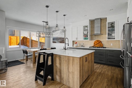 Two tone kitchen featuring two tone color scheme, a kitchen island with sink, dark wood-style flooring, backsplash, and hanging light fixtures - 34 Riverhill Crescent, St. Albert, AB - Indoor Photo Showing Kitchen With Upgraded Kitchen
