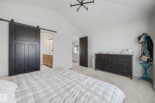 Bedroom featuring light colored carpet, a barn door, vaulted ceiling, and ensuite bathroom - 34 Riverhill Crescent, St. Albert, AB - Indoor Photo Showing Bedroom