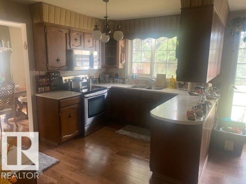 Kitchen with light countertops, a peninsula, stainless steel appliances, dark wood-style flooring, and suspended lighting - 206 Wolf Willow Crescent, Edmonton, AB - Indoor Photo Showing Kitchen With Double Sink