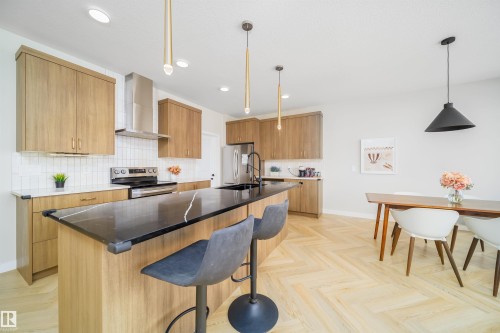 Kitchen featuring dark stone countertops, a breakfast bar area, stainless steel appliances, a kitchen island with sink, and parquet flooring - 15 Chambery Crescent, St. Albert, AB - Indoor