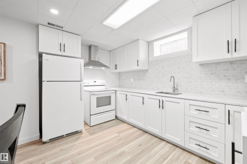 Kitchen featuring white appliances, white cabinetry, light wood-style flooring, light stone countertops, and decorative backsplash - 3429 120 Avenue, Edmonton, AB - Indoor Photo Showing Kitchen