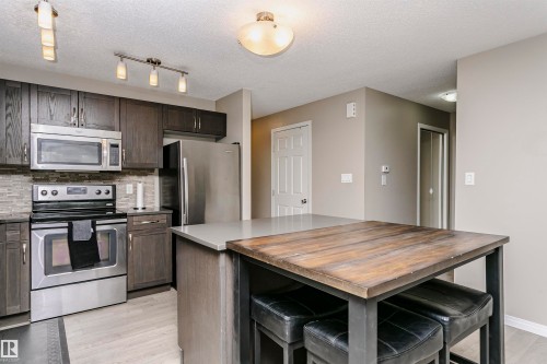 Kitchen featuring wood counters, stainless steel appliances, a breakfast bar, light wood-style flooring, and decorative backsplash - 4011 Orchards Drive, Edmonton, AB - Indoor Photo Showing Kitchen With Stainless Steel Kitchen