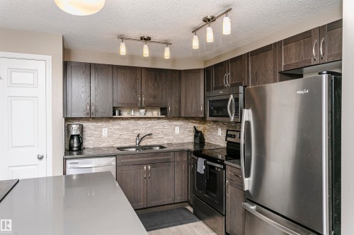 Kitchen featuring stainless steel appliances, dark wood finish cabinetry, open shelves, tasteful backsplash, and a textured ceiling - 4011 Orchards Drive, Edmonton, AB - Indoor Photo Showing Kitchen With Stainless Steel Kitchen With Double Sink With Upgraded Kitchen