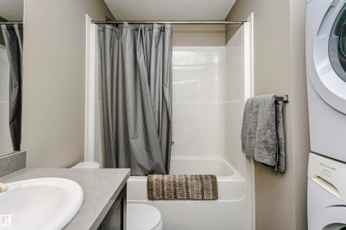 Bathroom featuring vanity, a textured ceiling, stacked washer / drying machine, and shower / bathtub combination with curtain - 4011 Orchards Drive, Edmonton, AB - Indoor