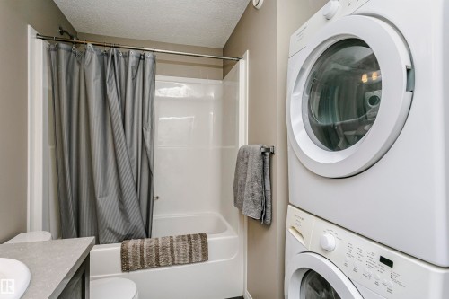 Laundry area with a textured ceiling and stacked washer and dryer - 4011 Orchards Drive, Edmonton, AB - Indoor Photo Showing Laundry Room